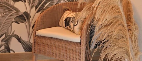 Una silla de mimbre con un cojín frente a una pared con un diseño de hojas tropicales.