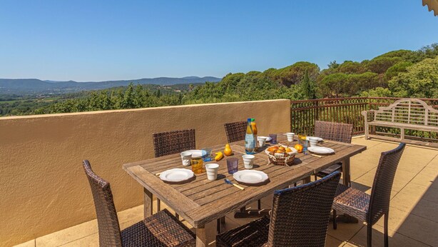 An outdoor dining area with a table set for four, surrounded by wicker chairs, overlooking a scenic landscape with hills and trees. - Lovely apartment for 6 guests with WIFI, A/C, TV, terrace and panoramic view (Grimaud)