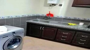 A compact kitchen with a washing machine, dark cabinets, and a tiled backsplash. - Residence Yasmine Mdiq 4691 (Mdiq)