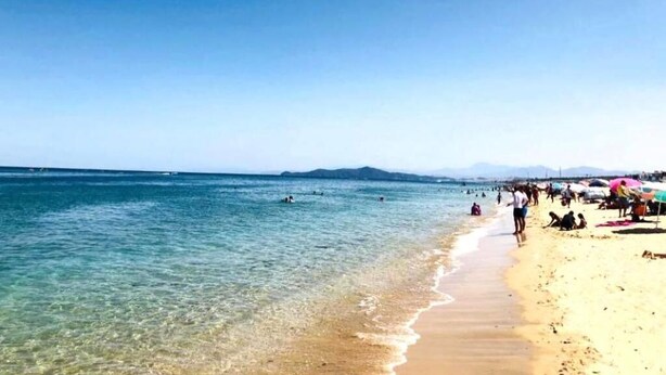 A beach with clear water, people swimming, and umbrellas on the sand. - Residence Yasmine Mdiq 4691 (Mdiq)