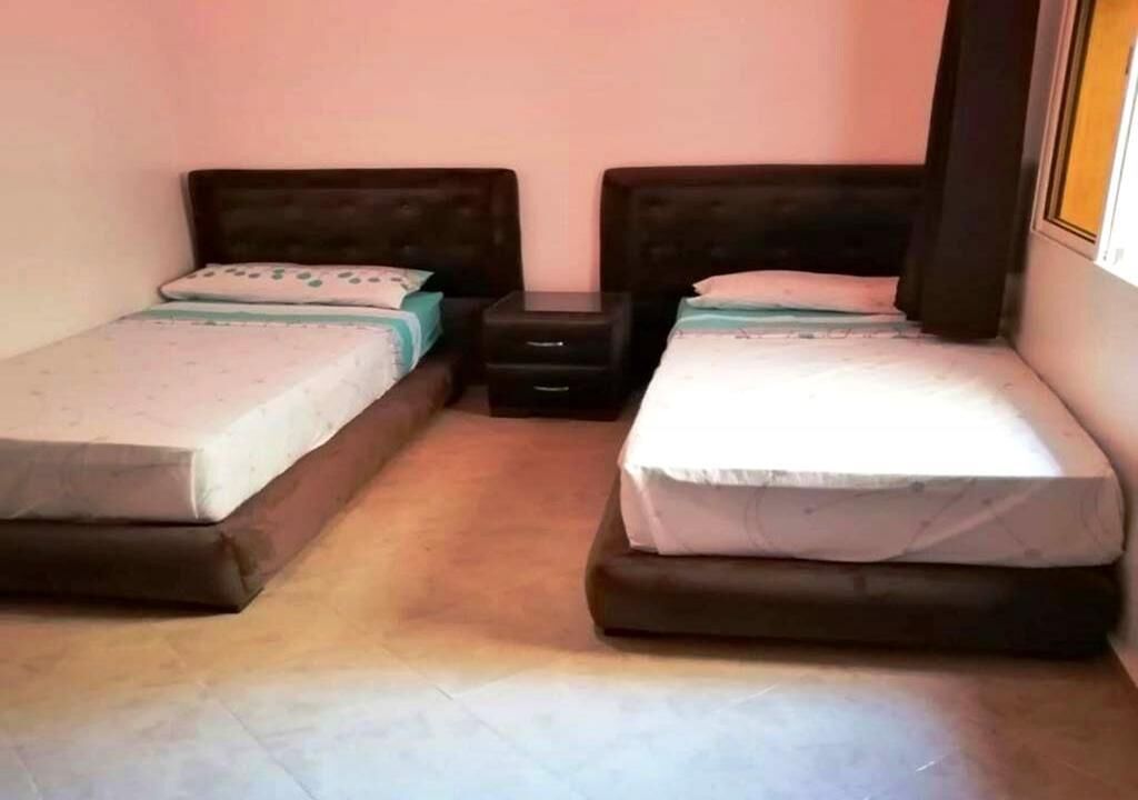 A small, clean room with two single beds, a nightstand, and a window.