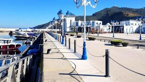 A coastal promenade with a row of white buildings, blue street lamps, and boats docked along the water. - Residence Yasmine Mdiq 4692 (Mdiq)