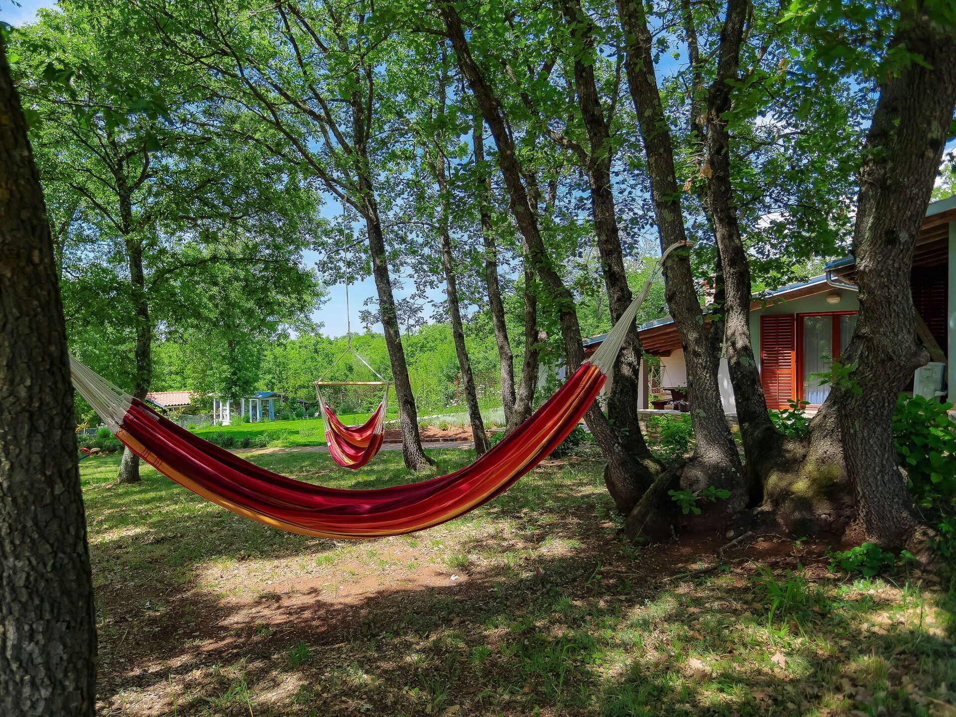 A hammock in a wooded area with trees and a building in the background.