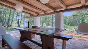 Eine hölzerne Pergola im Freien mit Tisch und Bänken, umgeben von Grünpflanzen.