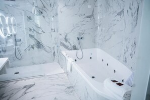 A modern bathroom with a marble wall, a bathtub, and a glass-enclosed shower area.