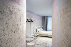Une chambre d’hôtel moderne avec un grand lit, une petite table, deux chaises et une lampe sur pied.
