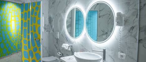 A modern bathroom with a white sink, two round mirrors, a handheld showerhead, and a toilet.
