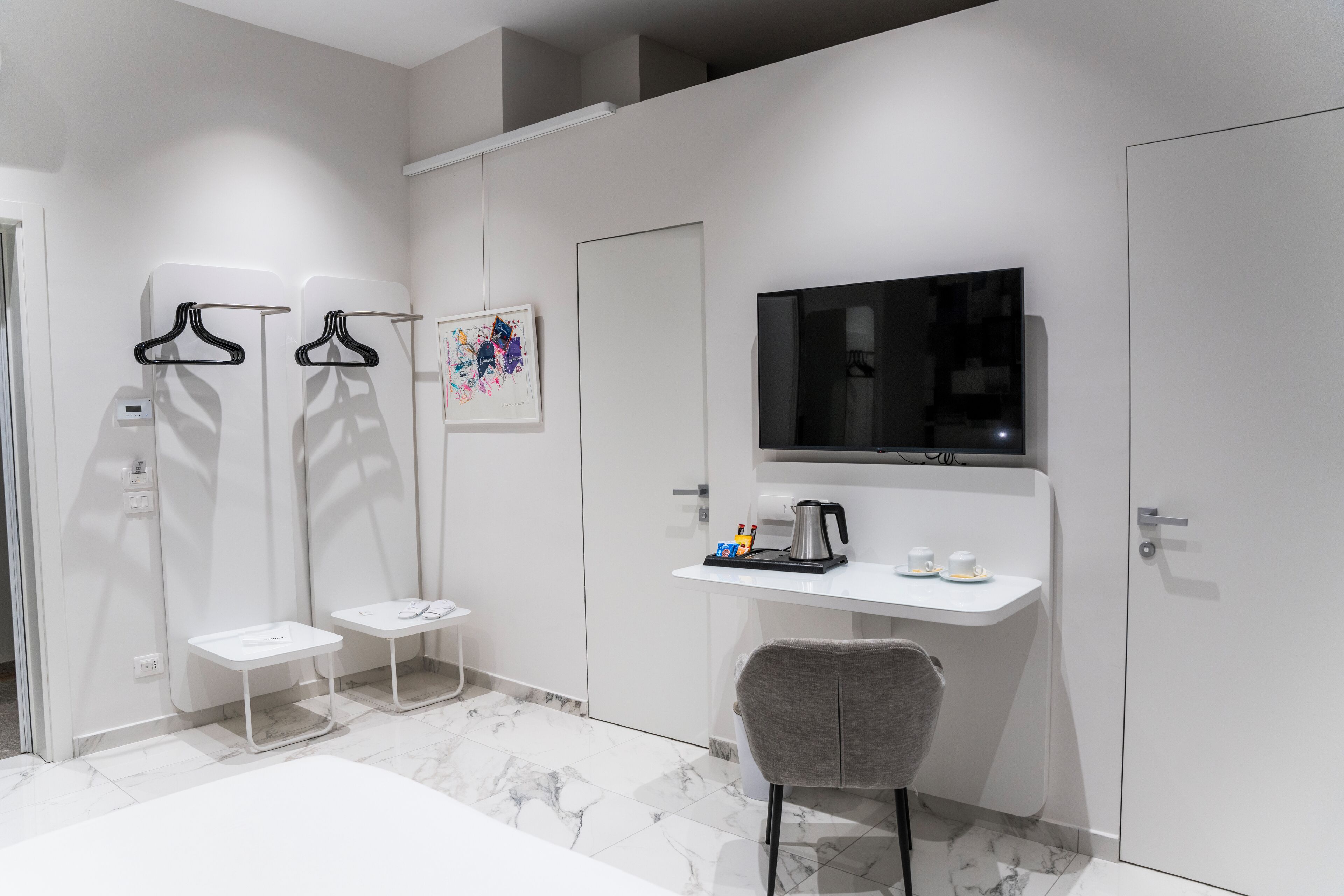 A modern bathroom with a white vanity, a chair, a TV mounted on the wall, and a shower area with towel racks.