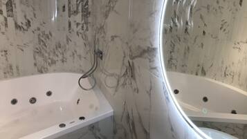 Une salle de bain moderne avec deux baignoires en marbre blanc, une douche à l’italienne et un mur en marbre.