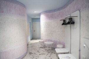 Un bagno moderno con pavimento in marmo, un tavolino bianco rotondo, una panca bianca e un porta asciugamani a parete.