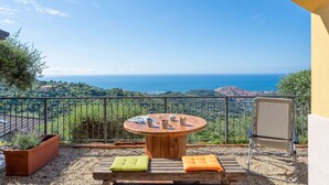 A balcony with a round wooden table, two cushioned chairs, and a view of the sea and hills. - Cosy apartment for 4 guests with WIFI, A/C, TV and patio (Imperia)