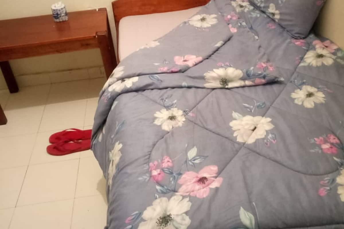 A bed with a floral duvet, a wooden headboard, and a nightstand with a cup.