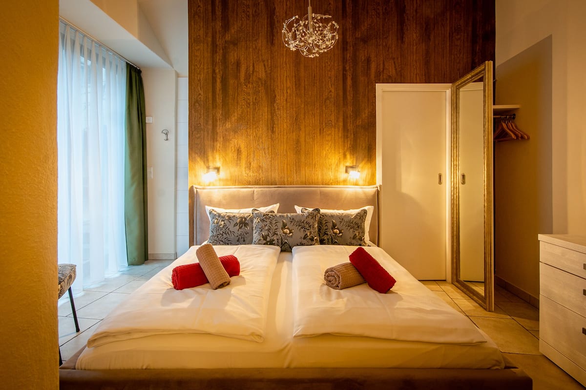 Quarto de hotel com uma cama grande, duas luminárias de cabeceira, uma cabeceira de madeira e um guarda-roupa.