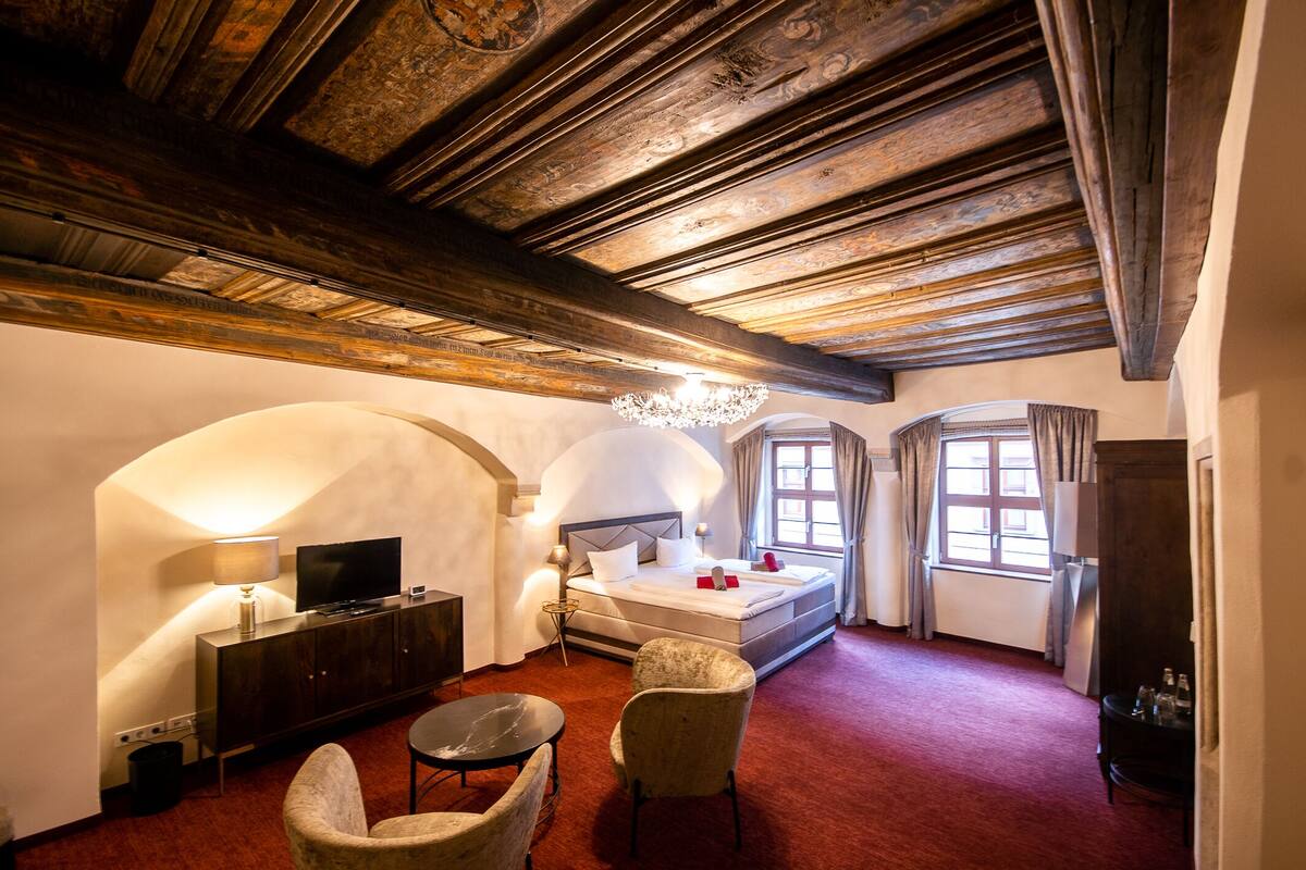 Quarto de hotel com teto de madeira, uma cama, uma TV, uma escrivaninha e uma cadeira.