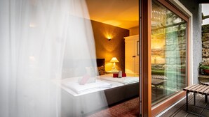 A bedroom with a bed, bedside table, lamp, and a view of the outdoors through a glass door. - Pension Donatus (Pirna)