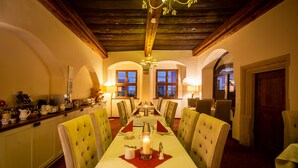 A dining area with a long table, green upholstered chairs, and a chandelier. - Pension Donatus (Pirna)