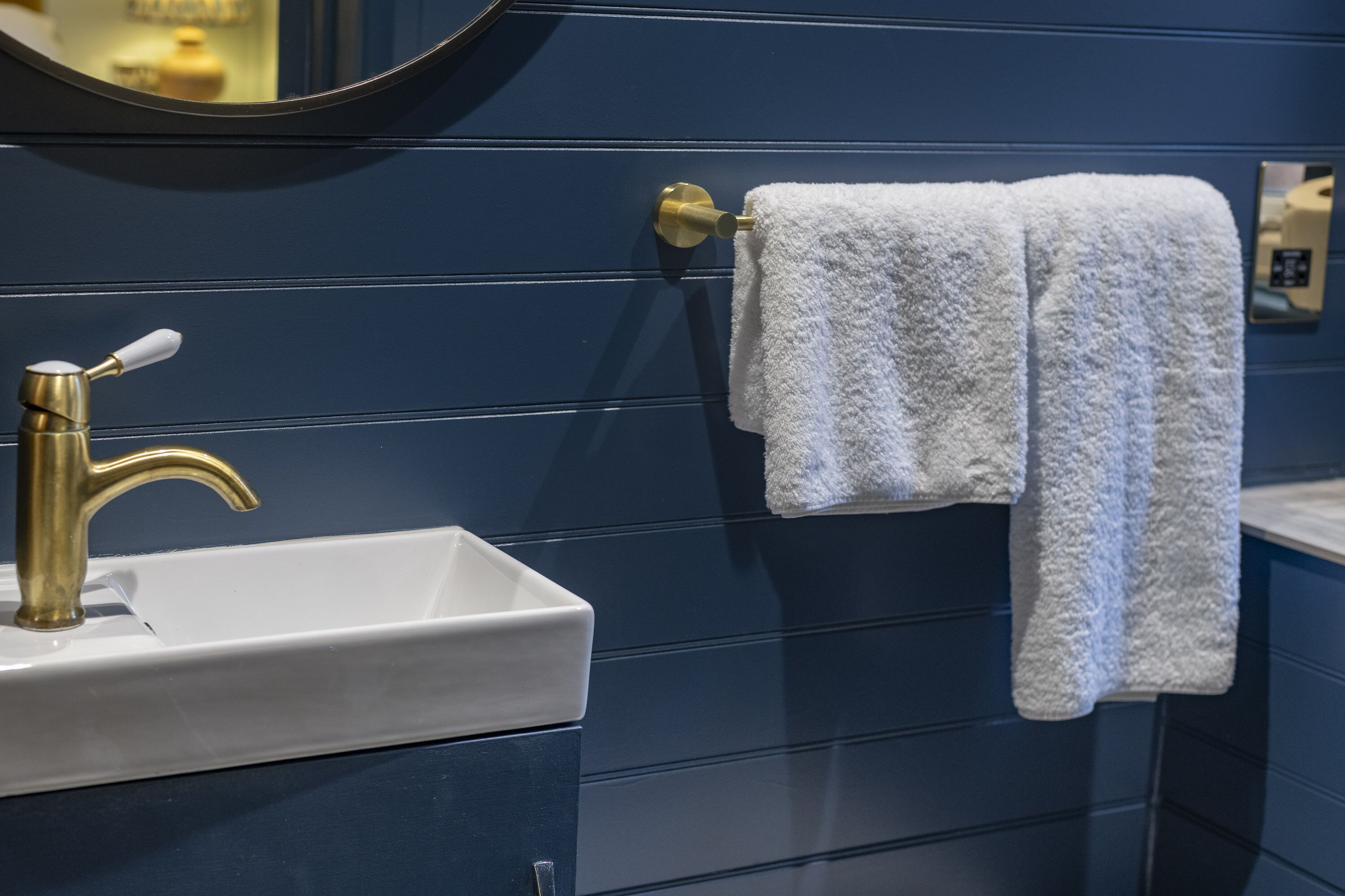 A bathroom with a white sink, gold faucet, and a towel hanging on a towel rack.