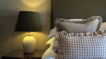 A neatly made bed with a checkered pillow and a plain pillow, a bedside lamp, and a dark-colored nightstand.