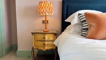Un lit avec une tête de lit bleue, une lampe de chevet avec un abat-jour à motifs et une petite table de chevet en bois dotée de tiroirs.