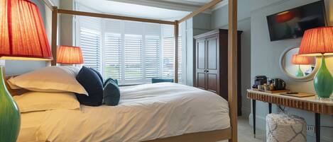 A four-poster bed with white linens, two red lamps, and a wooden nightstand.