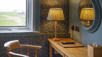 A room with a wooden chair, a desk with a lamp, a remote control, and a tissue box.