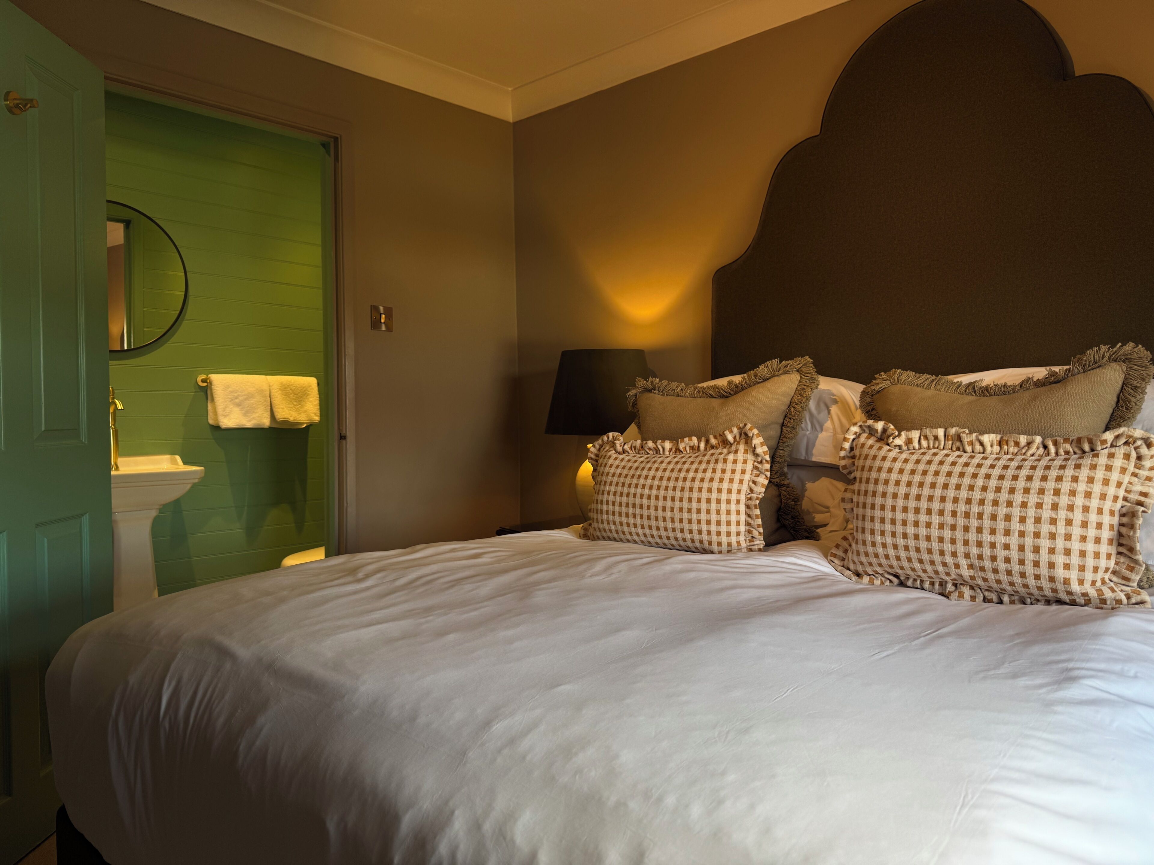 A hotel room with a bed, a green door, a sink, and a mirror.