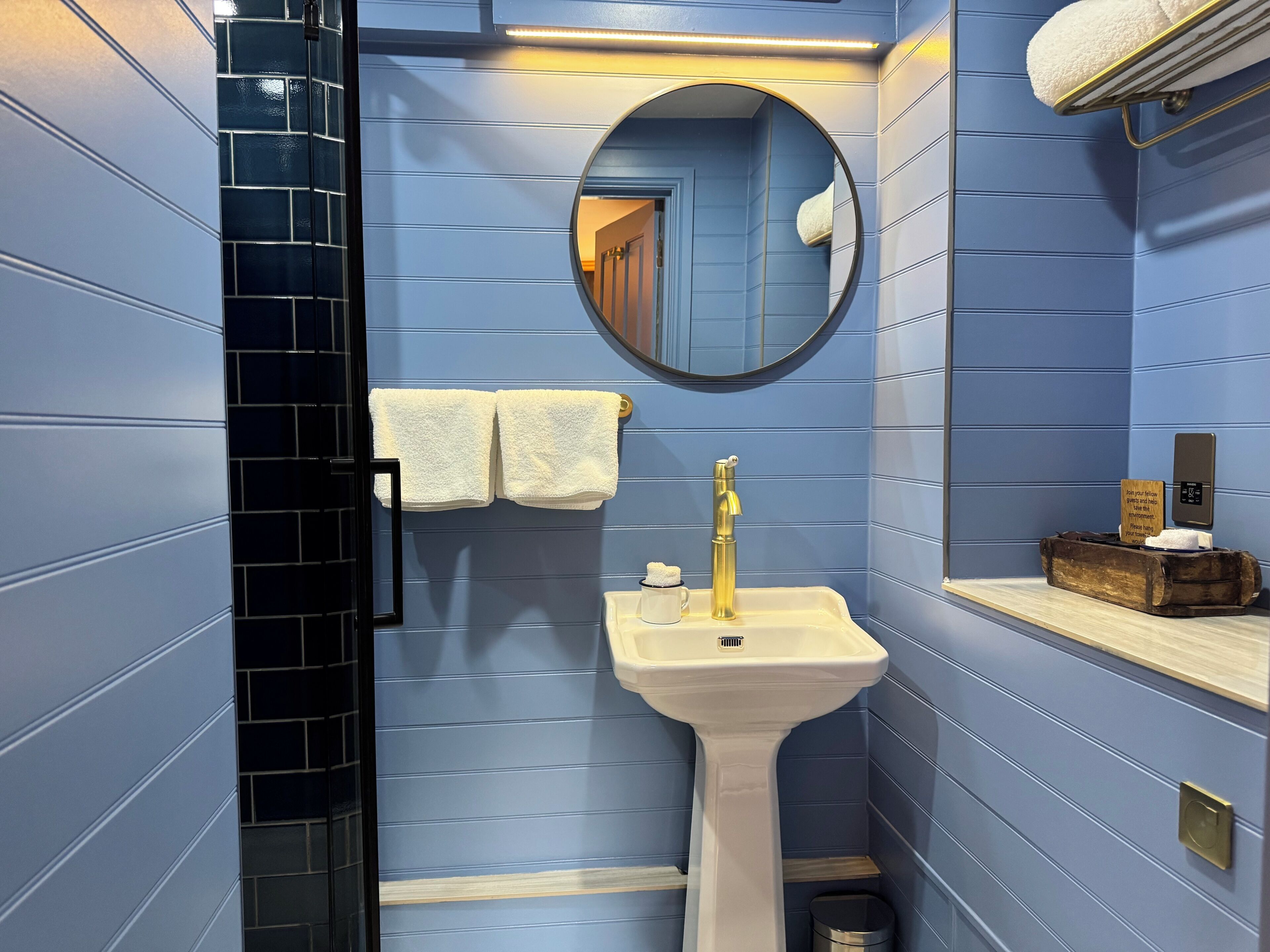 A bathroom with blue walls, a white sink, a gold faucet, a mirror, and a towel rack.