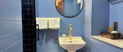 A bathroom with blue walls, a white sink, a gold faucet, a mirror, and a towel rack.