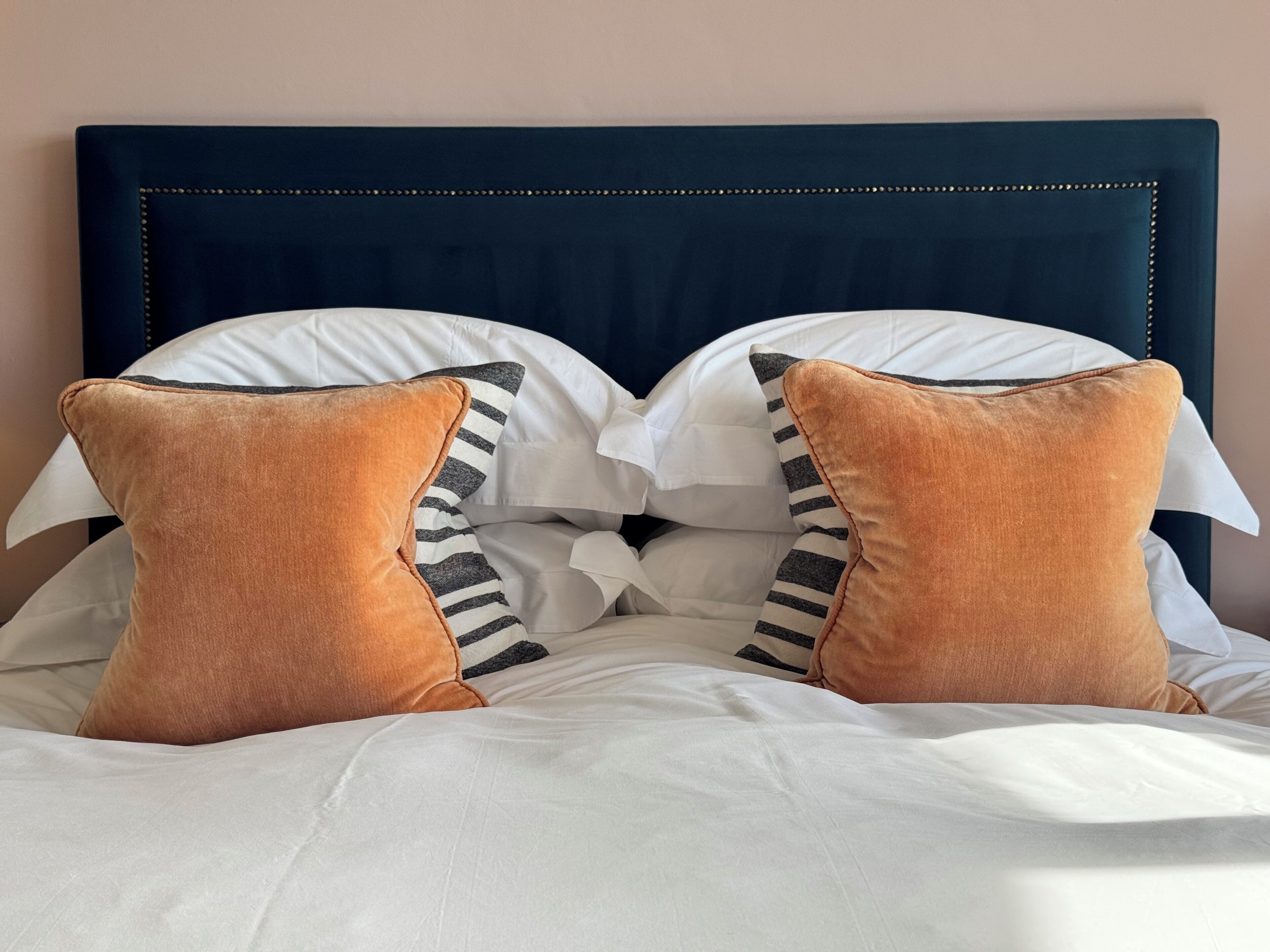 A bed with a dark headboard, white bedding, and two brown pillows with black stripes.