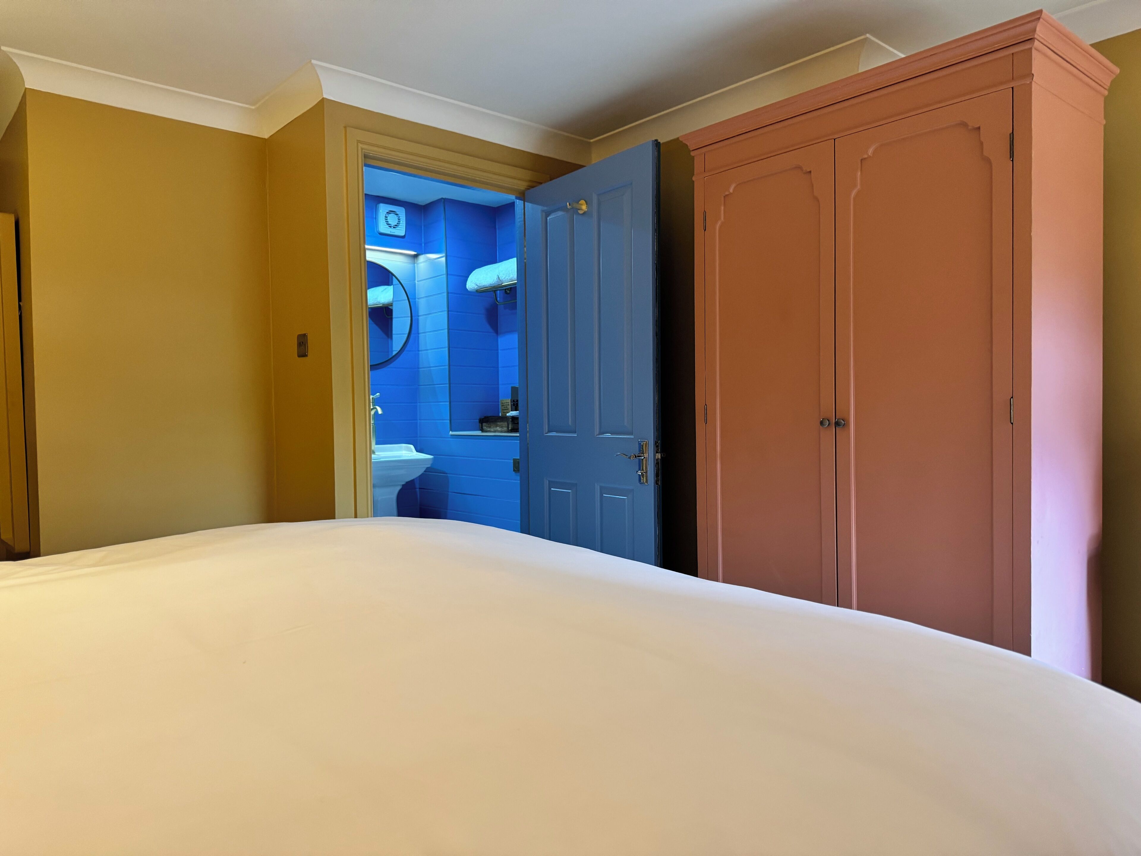 A hotel room with a bed, a wardrobe, and a bathroom visible through an open door.