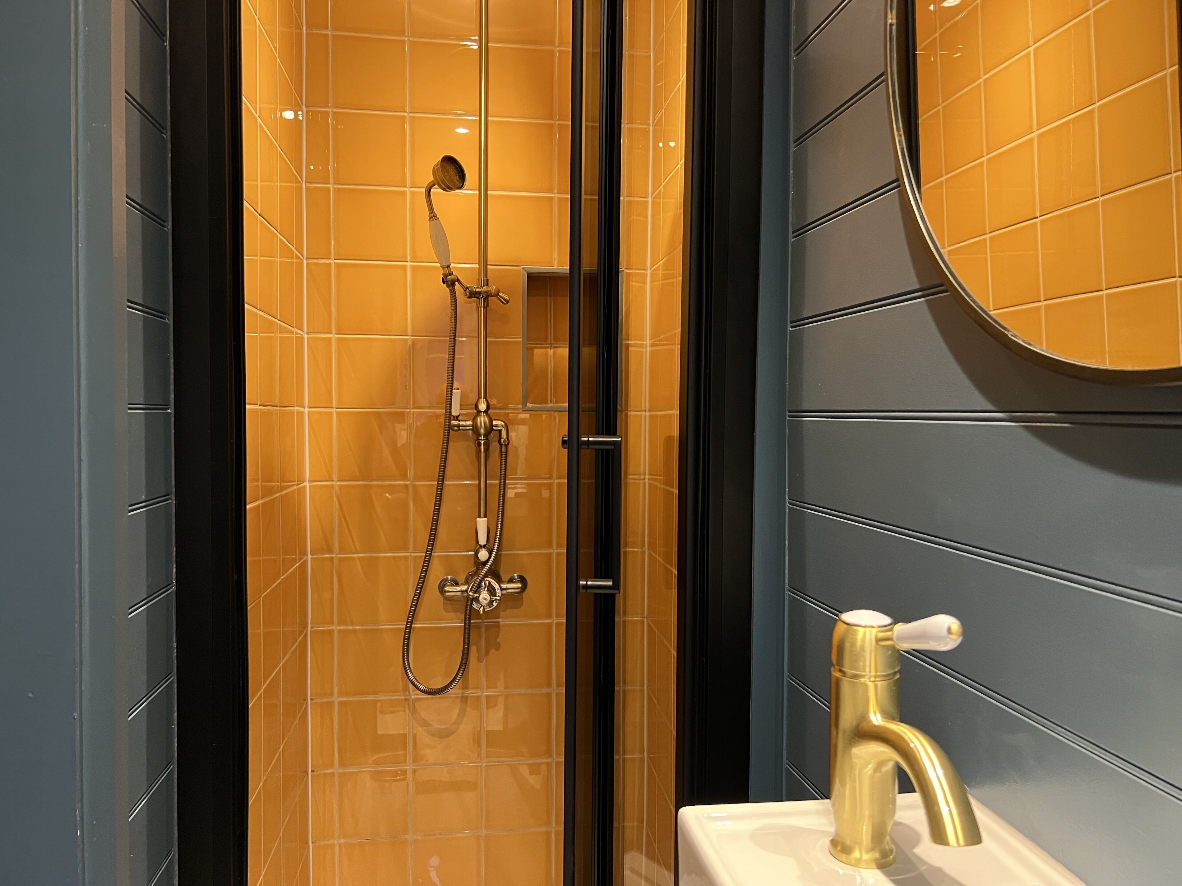 A modern bathroom with a glass-enclosed shower, a gold faucet, and a large mirror.