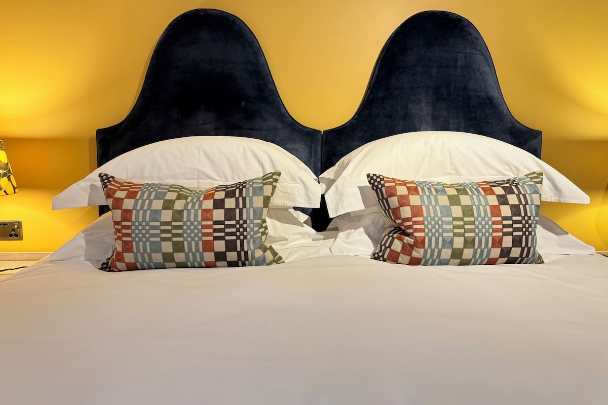 A double bed with a dark headboard, white bedding, and patterned pillows.
