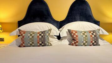 Una cama doble con cabecera oscura, ropa de cama blanca y almohadas estampadas.