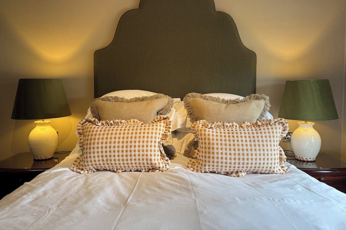 A neatly made bed with checkered pillows, two bedside lamps, and a dark headboard.