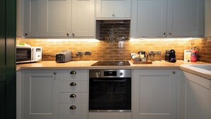 A kitchen with white cabinets, a microwave, toaster, oven, and a brick backsplash. - East Beach Guest House (Littlehampton)