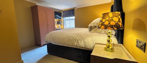 A bedroom with a bed, a bedside table, a lamp, a wardrobe, and a window.
