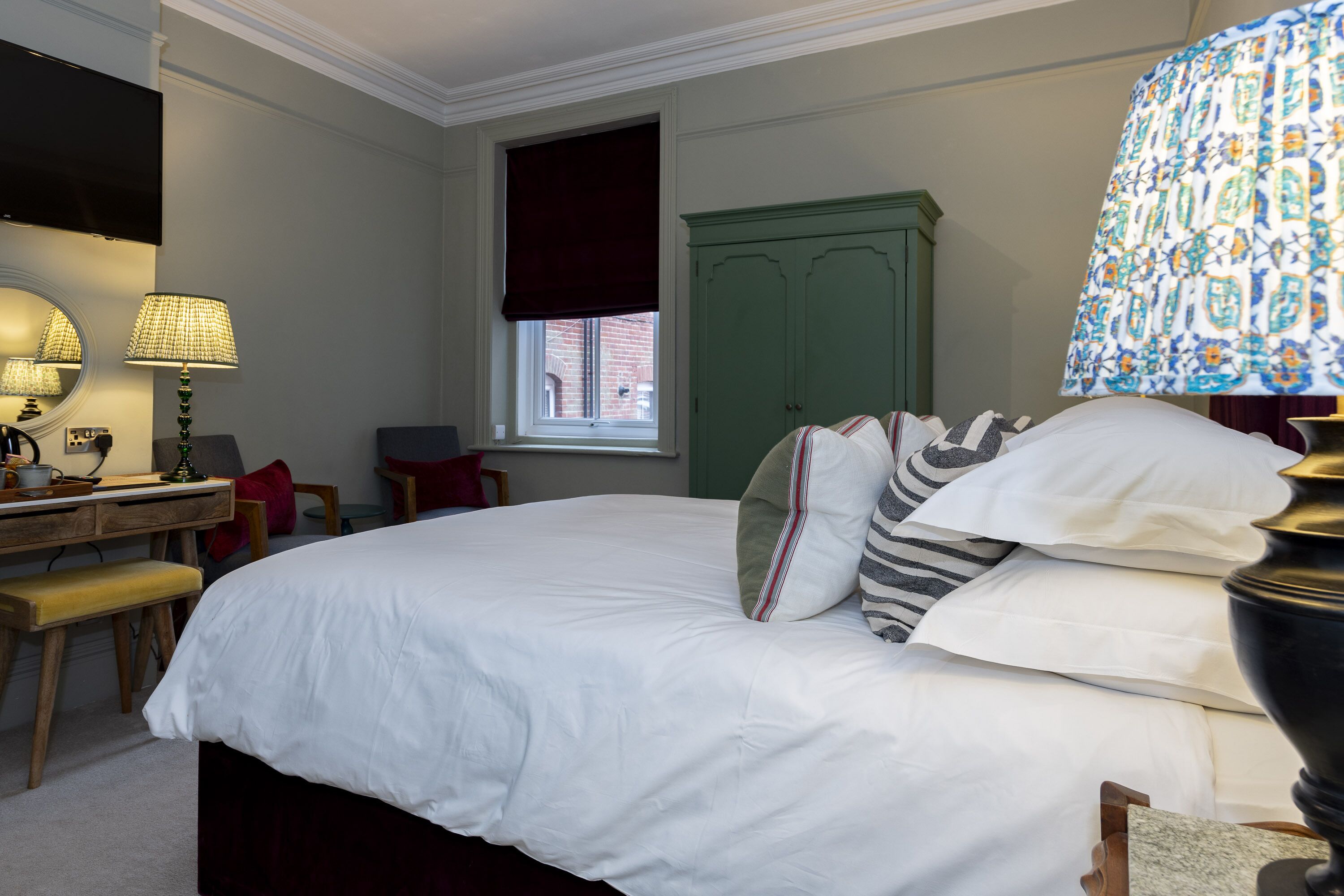 A neatly arranged bedroom with a bed, bedside table, lamp, and a green wardrobe.