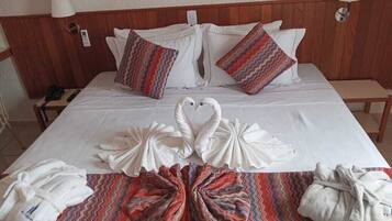 A neatly made bed with a heart-shaped towel arrangement, two patterned pillows, and a bedside table with a lamp.