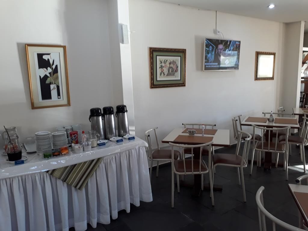 Un comedor con mesas y sillas, una mesa de buffet con recipientes de comida y bebida, y cuadros en las paredes.