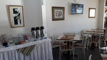 Un comedor con mesas y sillas, una mesa de buffet con recipientes de comida y bebida, y cuadros en las paredes.