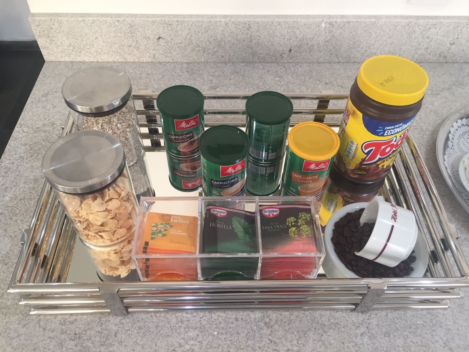 Una encimera de cocina con diversos alimentos y recipientes, entre ellos frascos de especias, un recipiente con granos de café y una bandeja con distintos productos alimenticios.