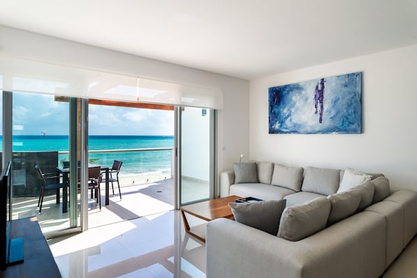 Ein modernes Wohnzimmer mit einem großen Glasfenster, das auf einen Balkon mit Meerblick führt.
