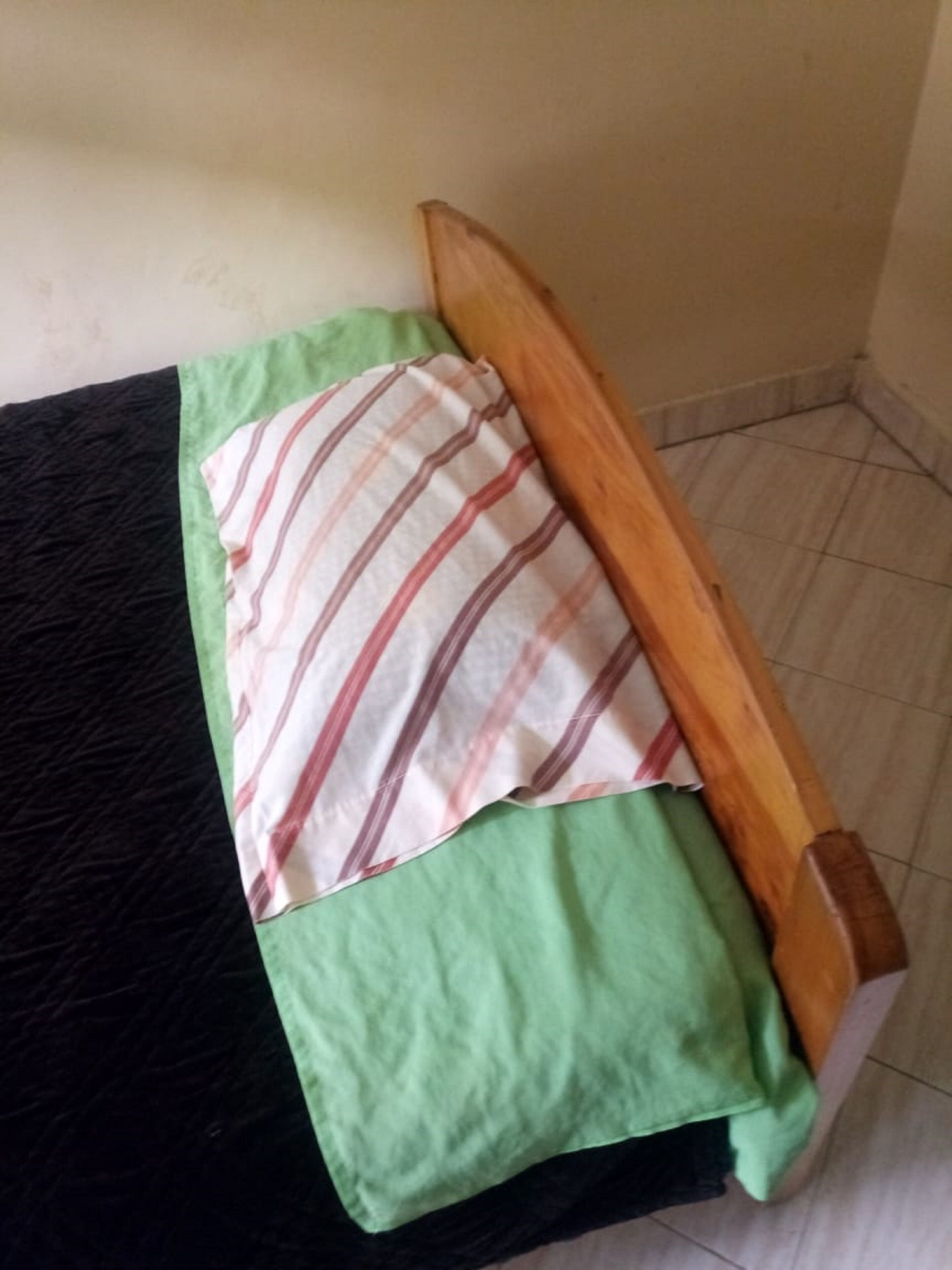 A small bed with a wooden frame and a green blanket.