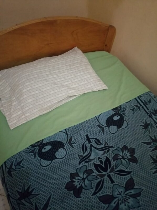 A bed with a wooden headboard, a white pillow, and a green and blue floral bedspread.