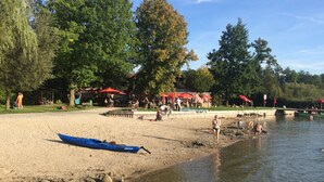 Un parque junto al lago con zonas de picnic, una playa de arena y un canoa azul.