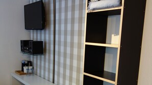 Habitación compacta con escritorio, asientos tipo banca, televisor montado en la pared y armario con estantes.