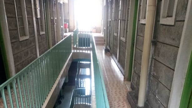Un pasillo con una escalera central, barandillas verdes y baldosas con diseños.