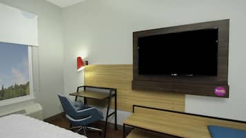 Habitación de hotel con cama, escritorio con silla, televisor montado en la pared y ventana con vista a árboles.