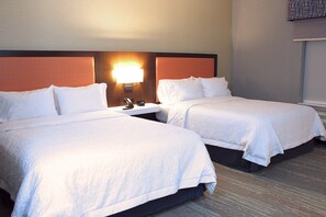 A hotel room with two beds, a nightstand, and a wall-mounted lamp.