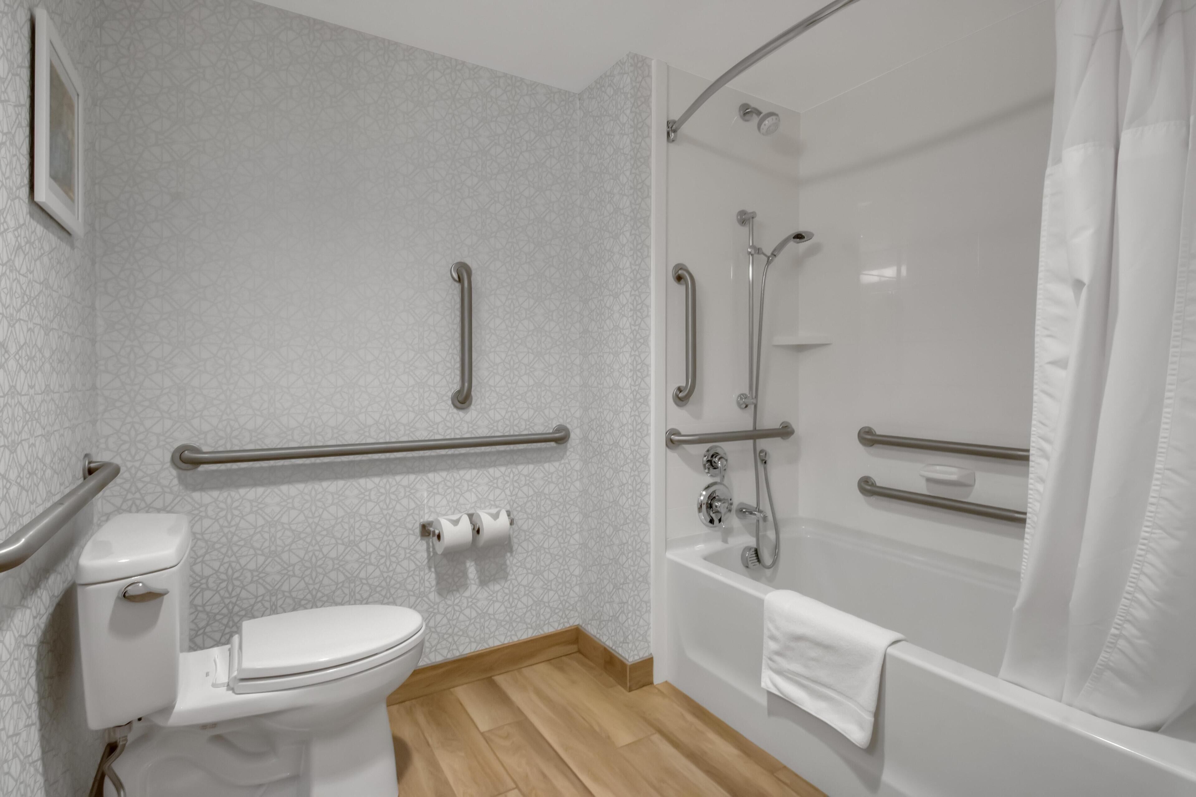 A bathroom with a toilet, a shower, and handrails.